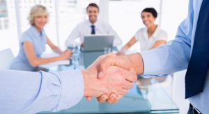 two men shake hands in front of three coworkers during a business meeting