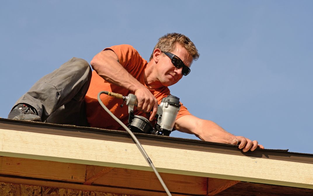 man in orange shirt and tinted safety glasses works on roof